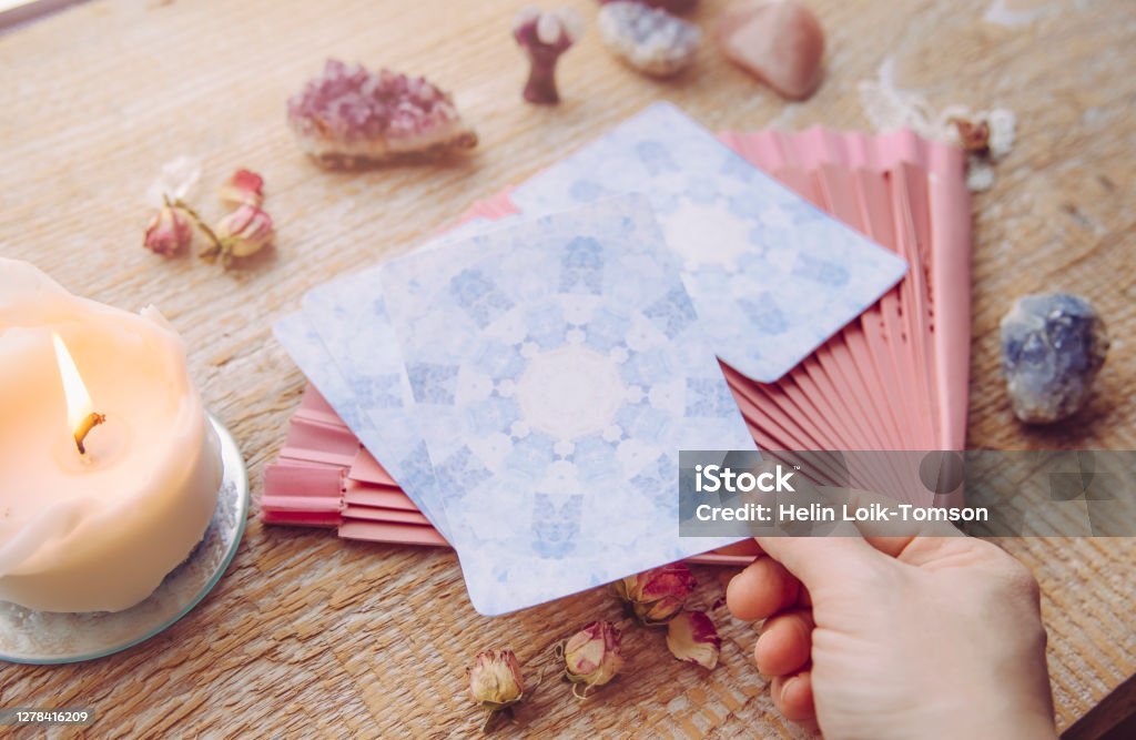 istockphoto-1278416209-1024×1024 Deck with divination homemade Angel cards on wood table, surrounded with semi precious stones crystals and candles. Person choosing picking a card.